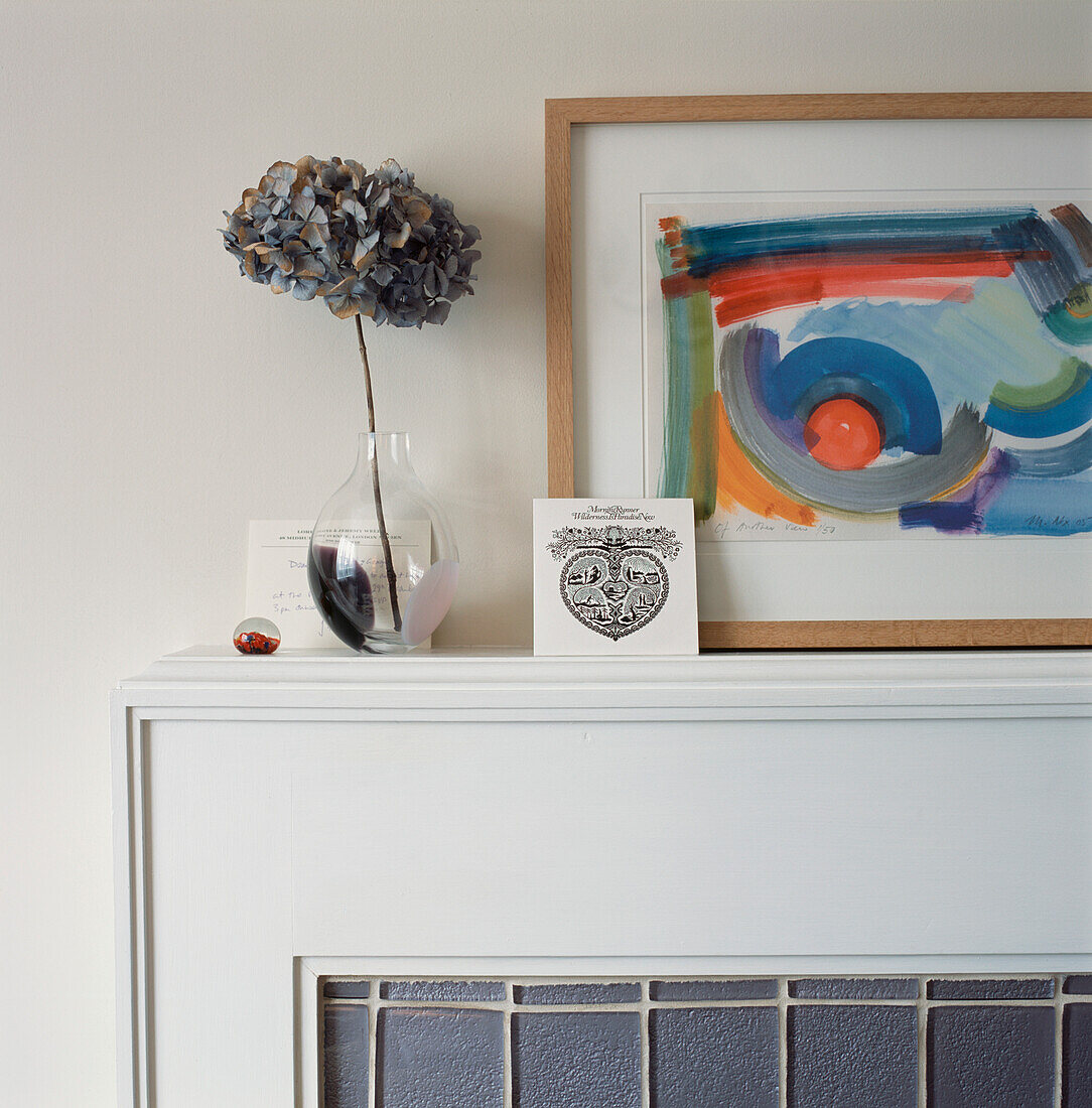 Weißer Kaminsims im Wohnzimmer mit graublauen Fliesen und Regal mit Bild und Hortensienblüten