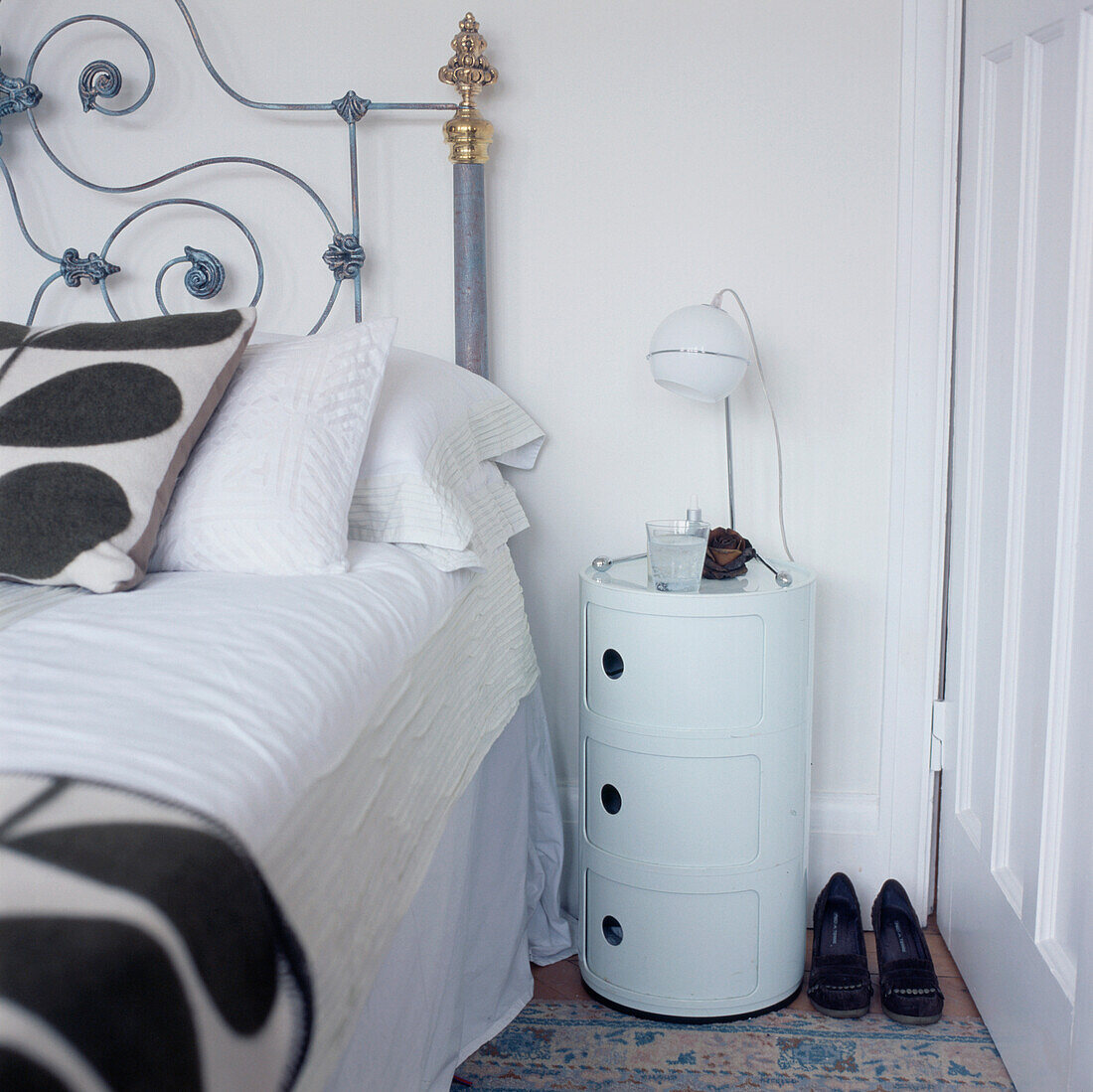 Weißes Schlafzimmer mit verschnörkeltem Bett im Vintage-Stil, schwarz-weiß gemusterter Bettwäsche und einem weißen Nachttisch