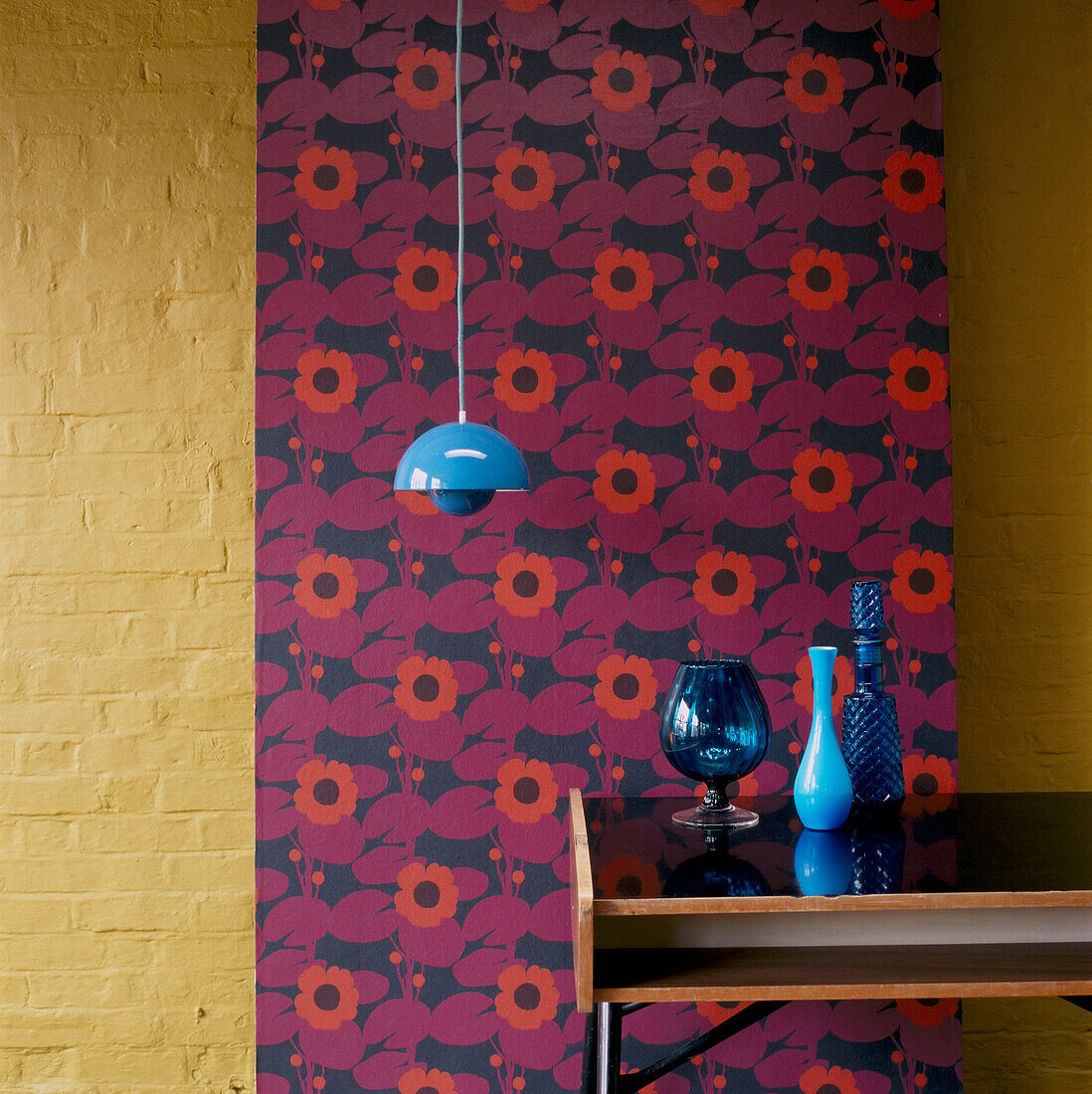Panel of patterned wallpaper against a painted brick wall side table and home wares