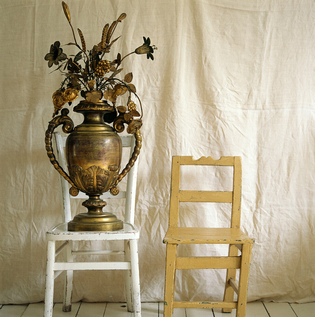 Zwei nicht zusammenpassende, lackierte Holzstühle, goldfarbene Urne mit goldbesprühten Blumen