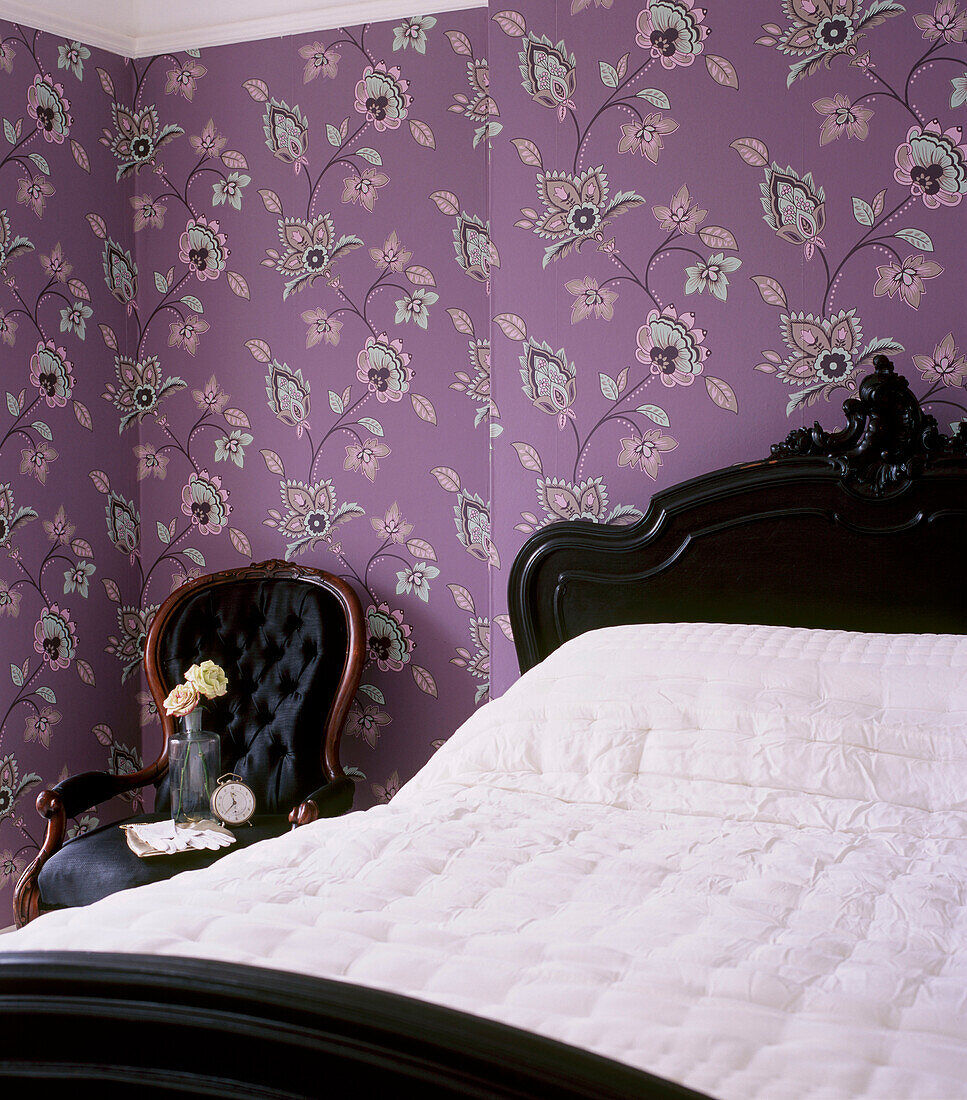 Schlafzimmer mit bunter Mustertapete und verschnörkeltem schwarzen Doppelbett mit weißer Bettwäsche