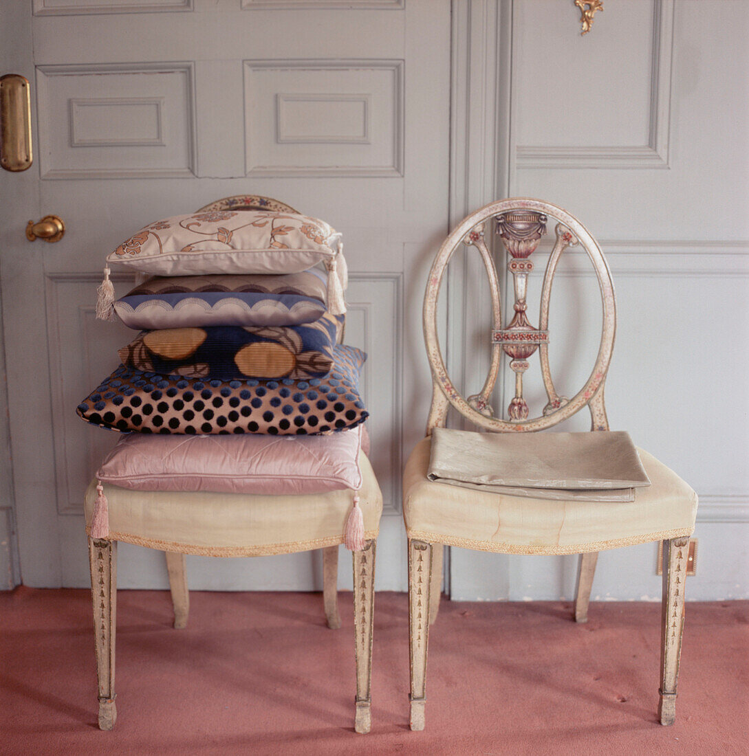 Zwei Regency-Stühle mit einem Stapel Kissen vor einer getäfelten Wand und einer Tür
