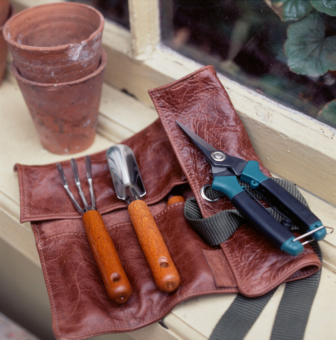 Leather pouch containing gardening and planting tools resting on a window ledge 