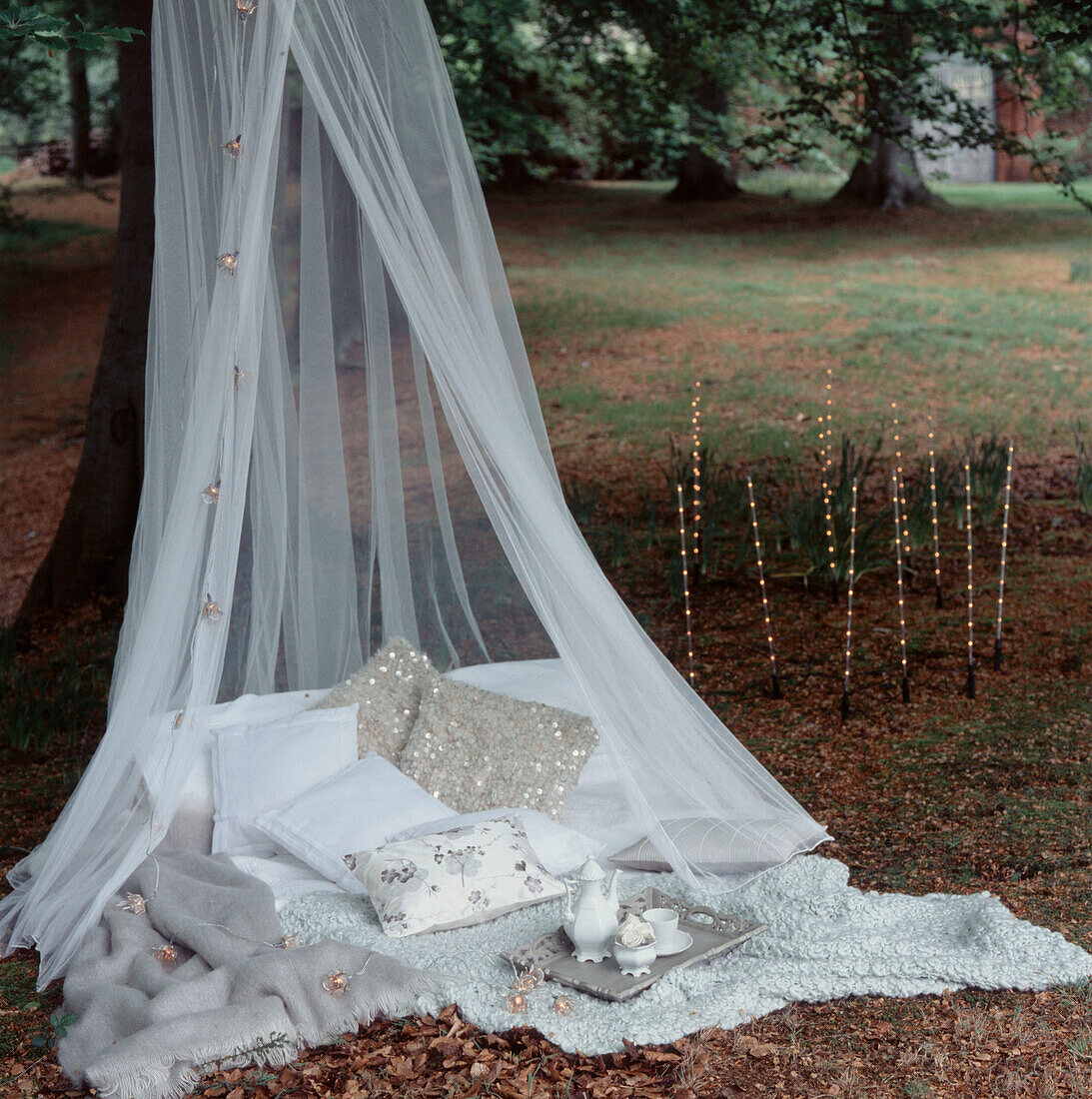 Romantic picnic setting in the woods with cushions blankets and fairy lights