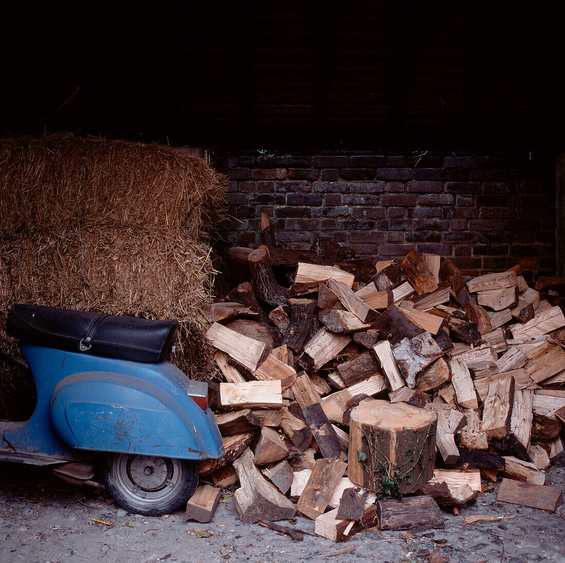 A log pile moped and a hay stack in an old brick barn