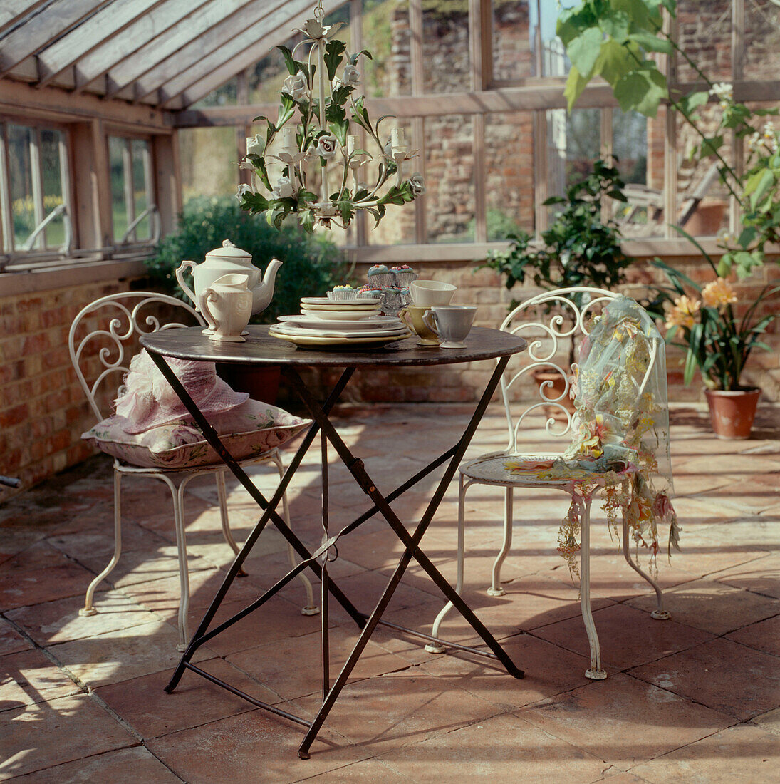 Gartentisch und Stühle aus Metall in einem historischen Glaswintergarten mit Tafelgeschirr