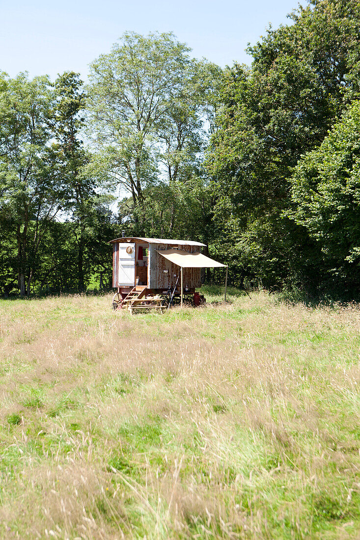 Eine Schäferhütte auf einer Sommerwiese mit einem Zeltdach für eine provisorische Essküche und einer offenen Tür mit Stufen zum Innenraum