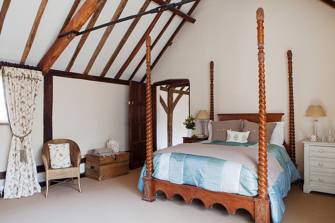 Carved four poster bed in beamed room of Surrey barn conversion England UK