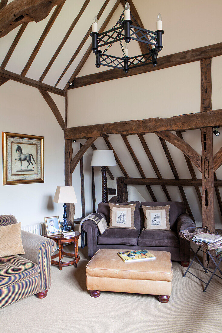 Zweisitzer-Sofa mit Leder-Ottomane im Balken-Wohnzimmer einer umgebauten Scheune in Surrey, England UK
