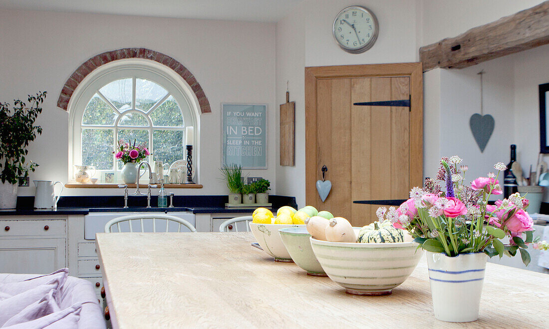 Fruit bowls on wooden kitchen table with arched window in Surrey cottage England UK