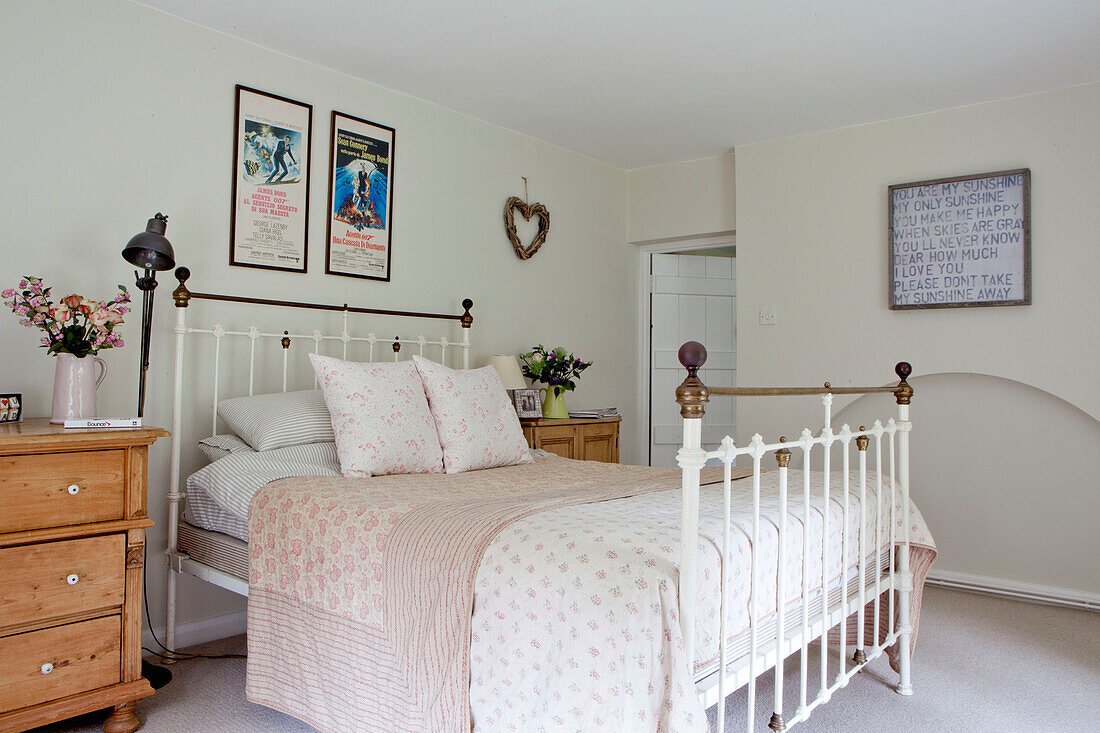 Brass bed and artwork with wooden chests of drawers in Surrey cottage England UK