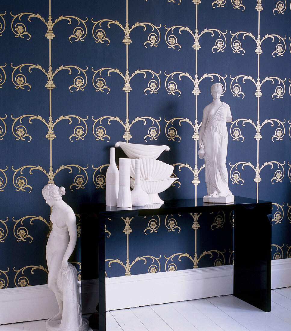 Blue and gold patterned wallpaper in a hallway with black console table displaying white ceramic homeware