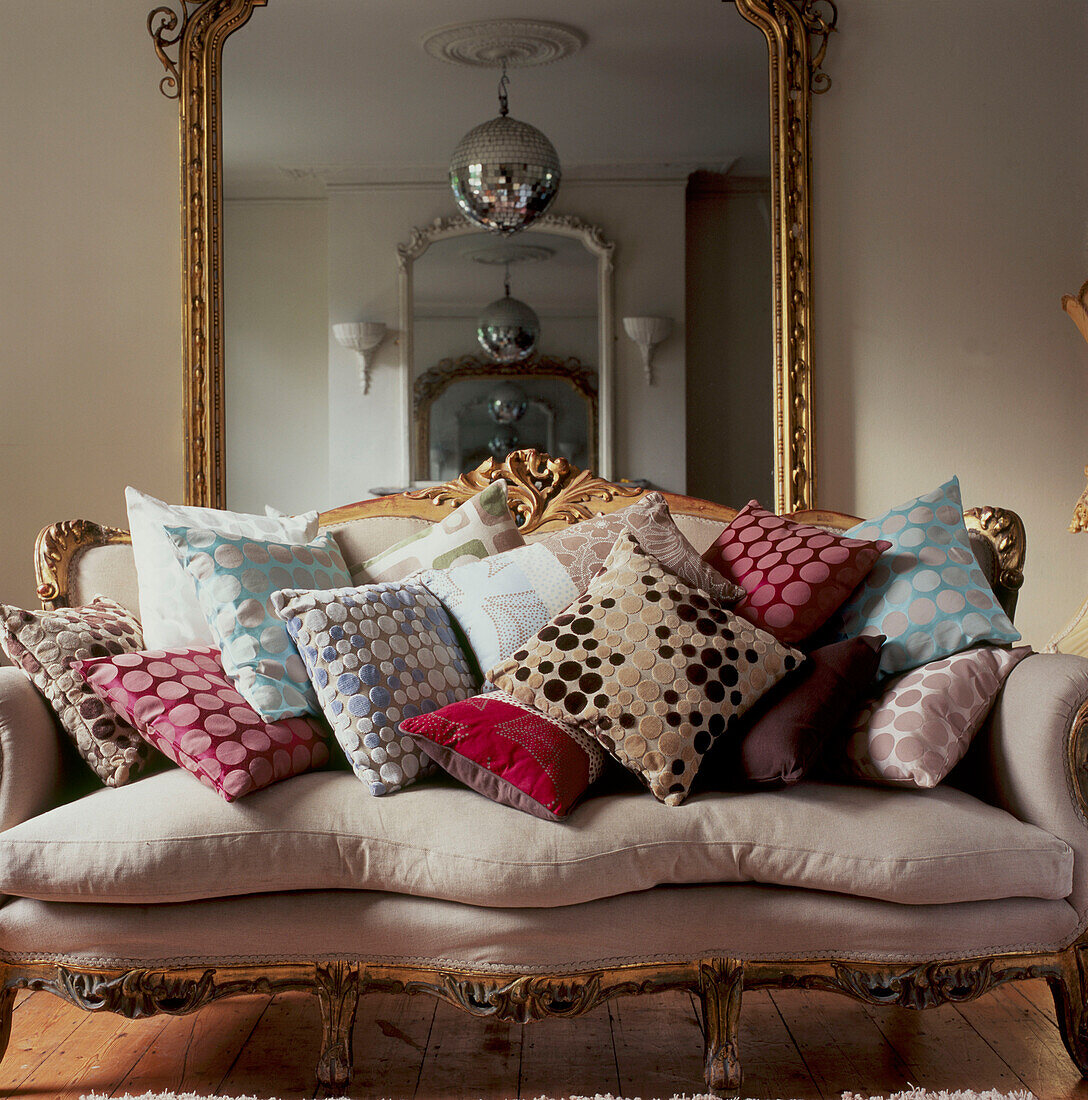 Decorative upholstered vintage sofa piled with patterned fabric cushions in a living room with large mirror