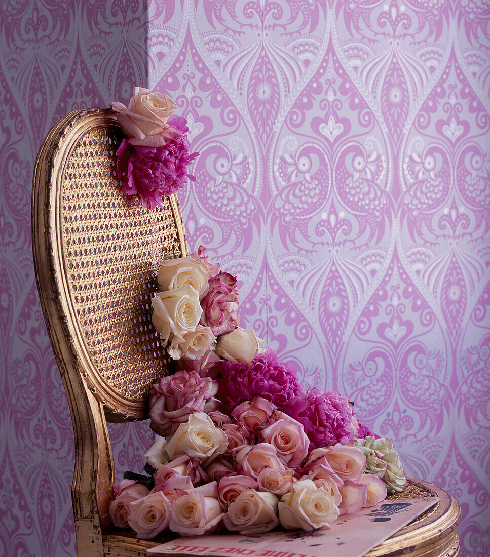 Pink bold patterned wallpaper with gold painted chair and flower display