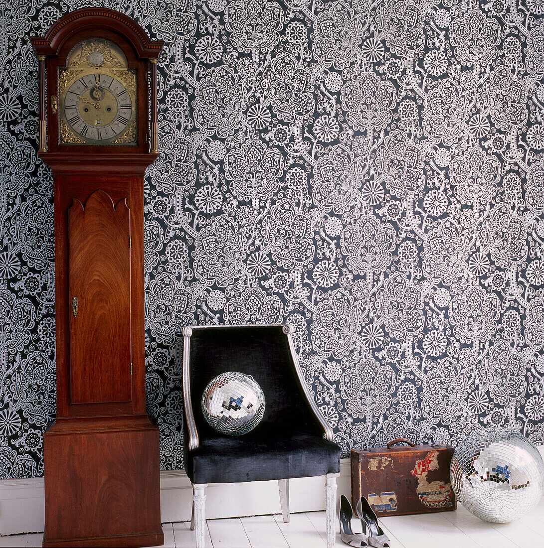 Bold patterned wallpaper in a hallway with grandfather clock upholstered chair shoes suitcase and disco balls