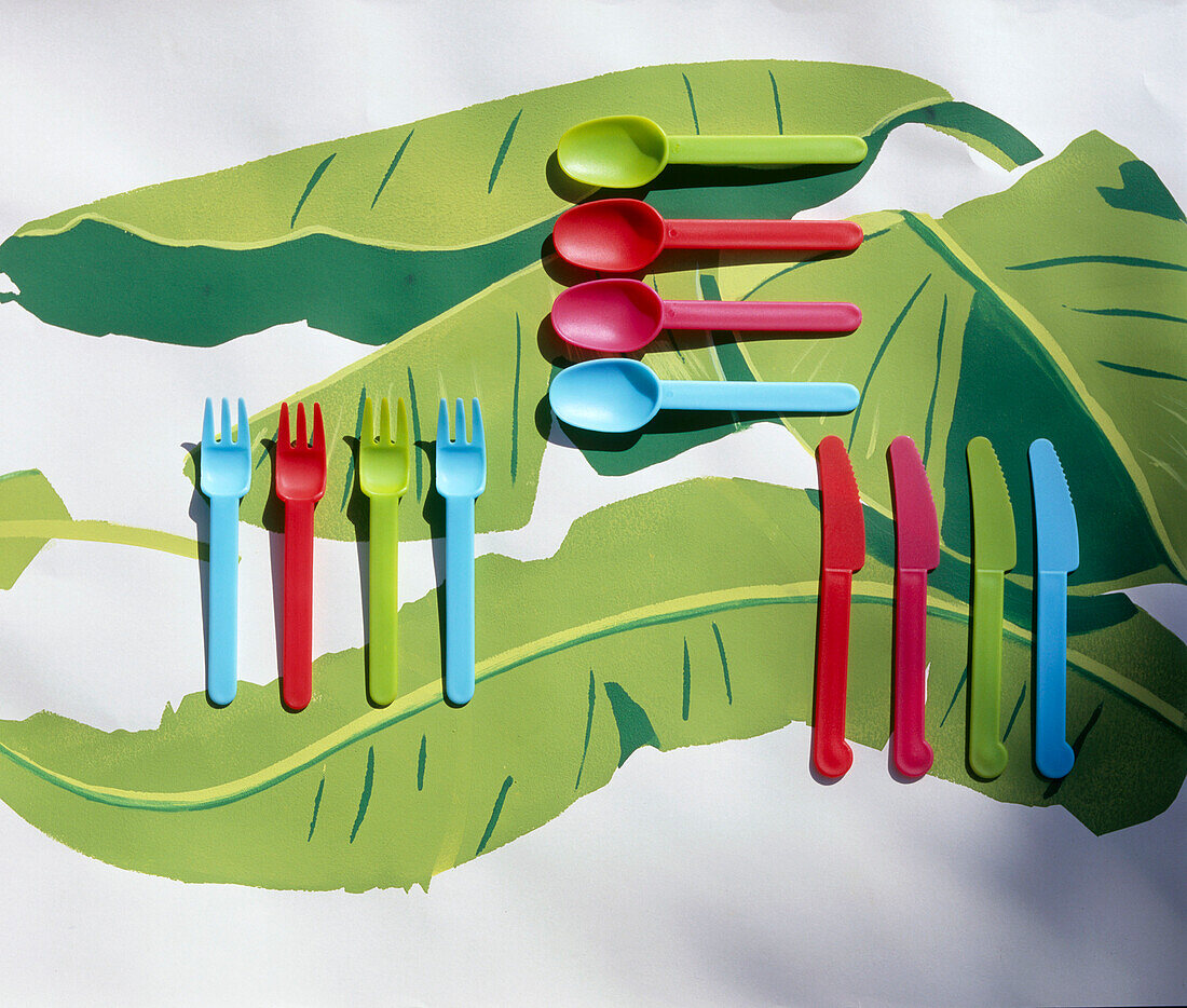 Coloured plastic cutlery on a leaf patterned tablecloth