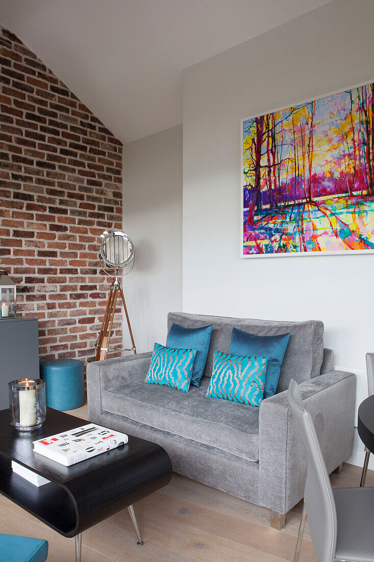 Grey sofa with blue cushions beside exposed brickwork in a modern apartment