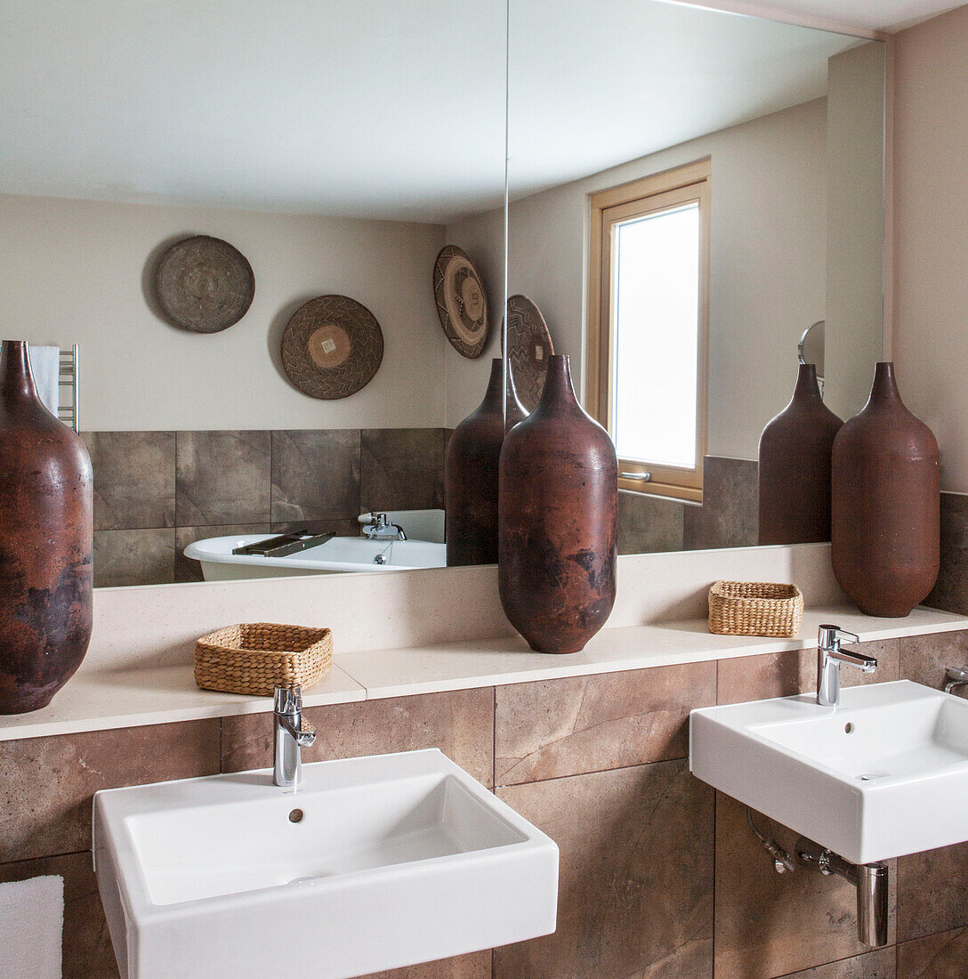 Large earthenware urns against mirrored wall above double basins in Lakes bathroom, England, UK