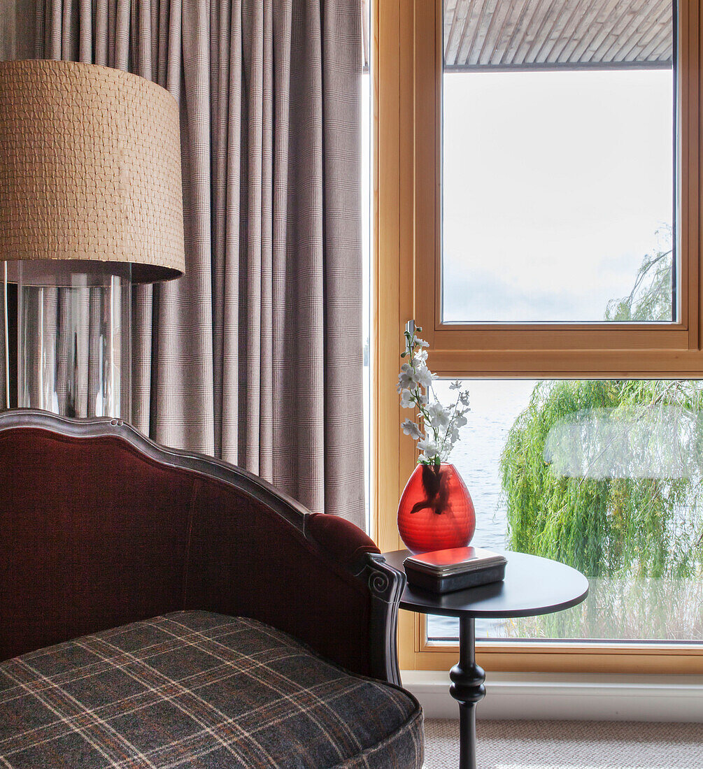 Schnittblumen in roter Glasvase mit gepolstertem Sitz am Fenster eines Hauses in Lakes, England, UK