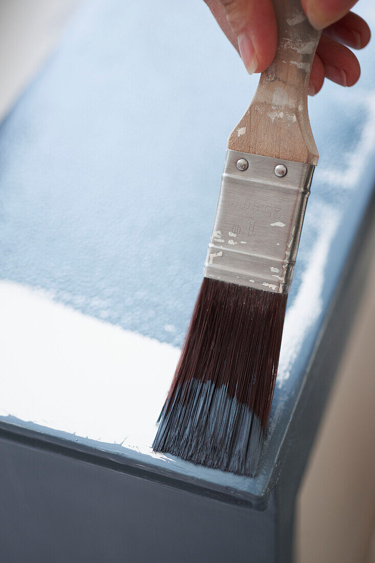 Paintbrushing edges of sideboard in UK home