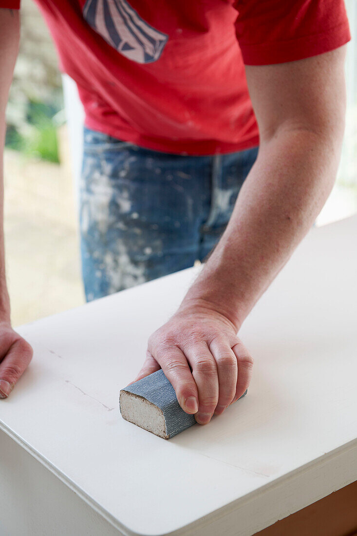 Man works with sanding block on sideboard in UK home