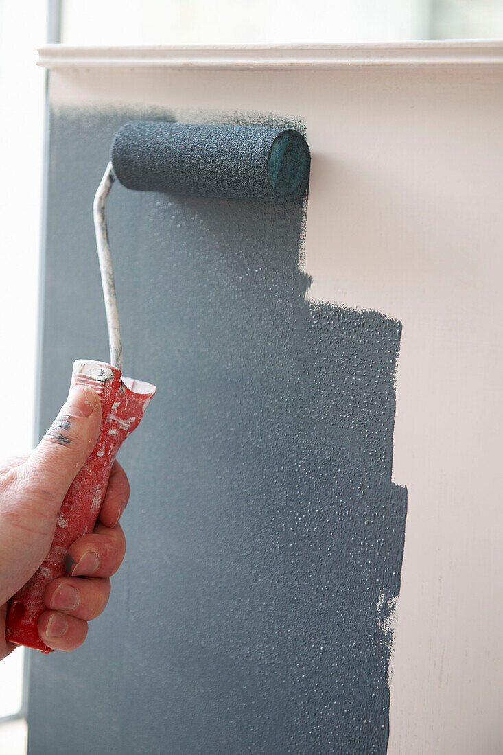 Man roller painting wall in UK home
