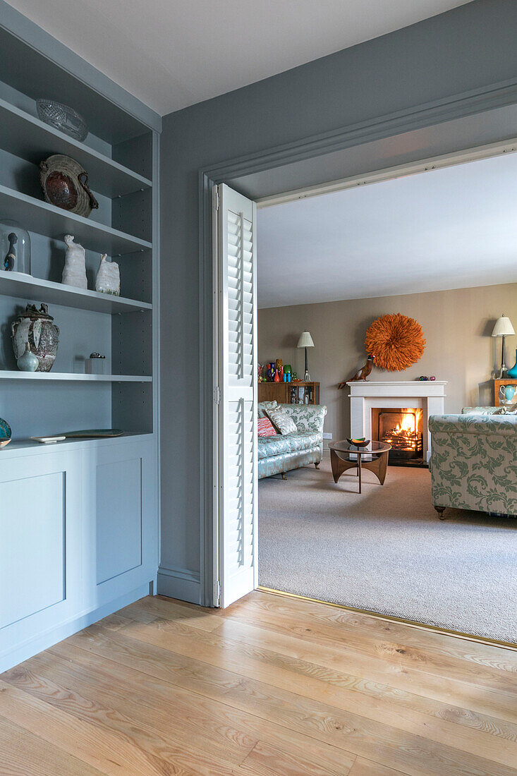 Light blue shelving with view through doorway to living room with lit fire in Farnham home Surrey UK