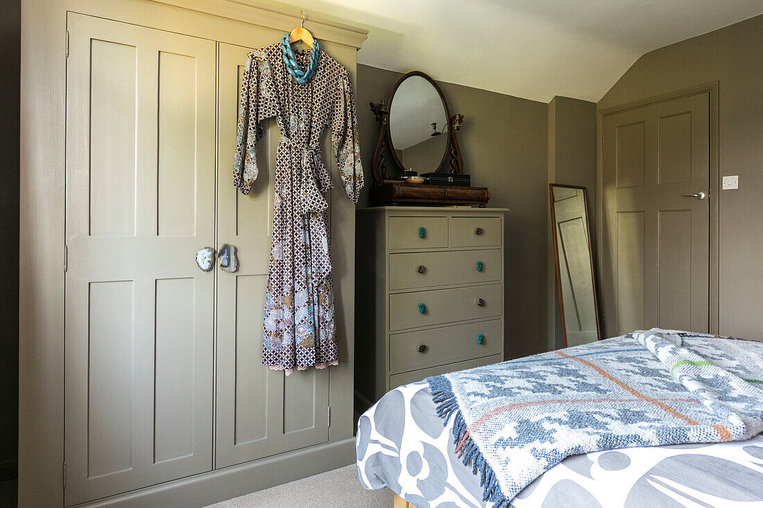 Vintage-Kleid hängt mit antikem Spiegel an Tallboy in Schlafzimmer in Farnham Surrey UK