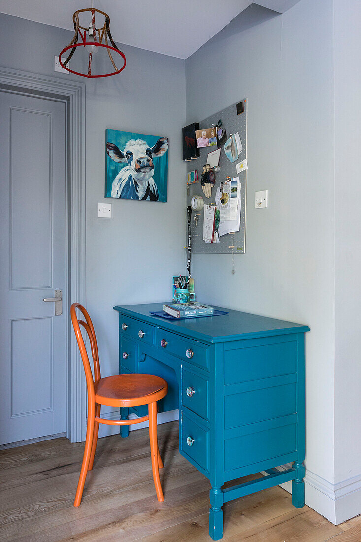 Orangefarbener Stuhl an blauem Upcycling-Schreibtisch mit Kunstwerken und Pinnwand in einem Haus in Farnham, Surrey, UK