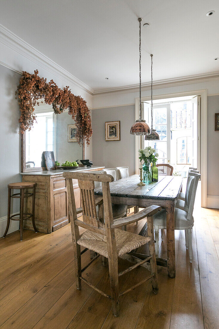 Esstisch und Stühle aus Holz mit Trockenblumen auf einem großen Spiegel in einem Haus in Winchester UK