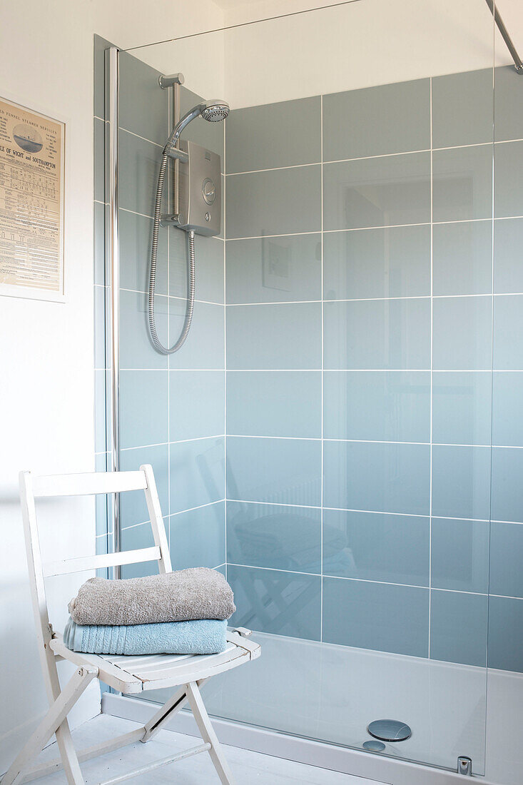 Gefaltete Handtücher auf einem Stuhl mit glasgefliester Duschkabine in einem Haus auf der Isle of White