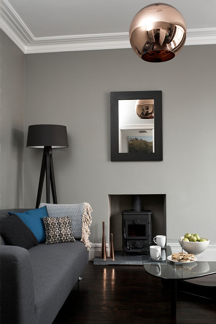 Metallischer Lampenschirm im Wohnzimmer mit Holzbrenner und grauem Sofa