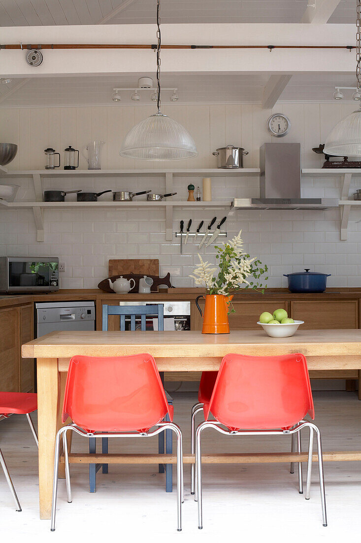 Red plastic chairs at wooden table in tiled kitchen with open shelving