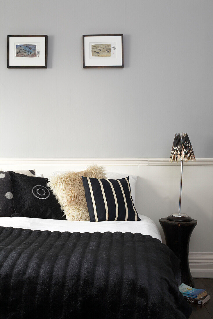 Schwarzer Bettbezug mit kontrastierenden Kissen unter zwei Kunstwerken