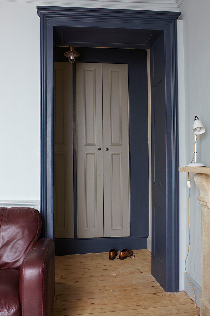 Pair of shoes on wooden floor viewed through blue painted doorframe in contemporary Bristol home, England, UK