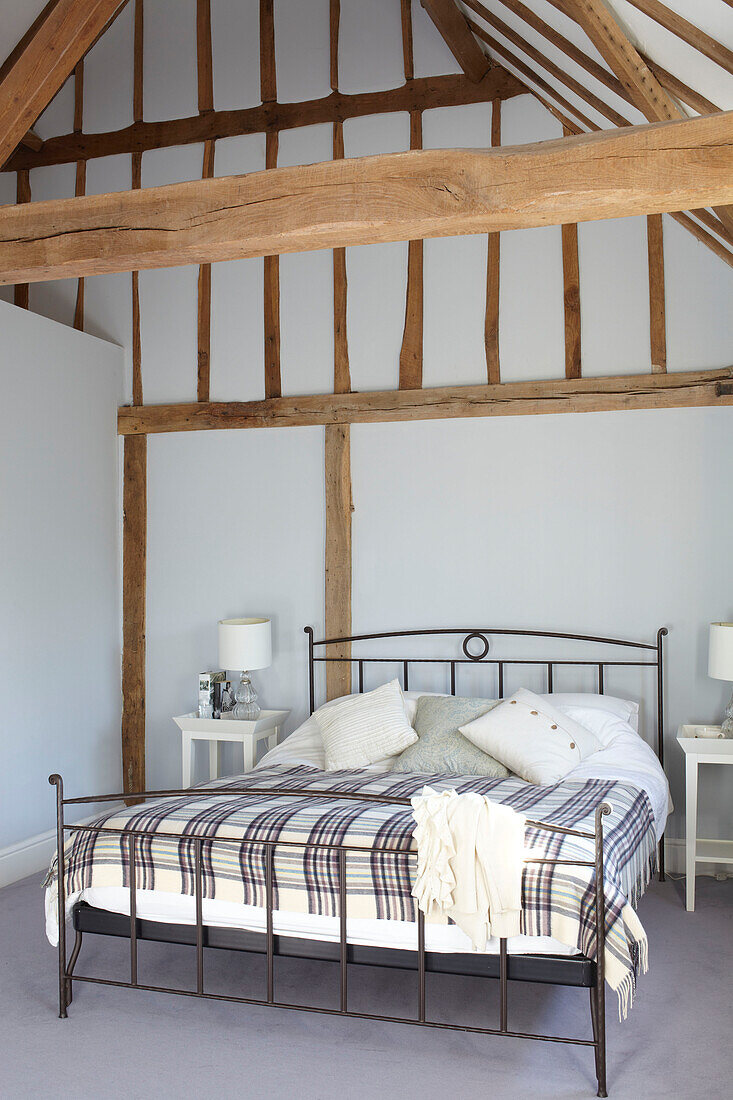 Metal framed bed in high timbered room of Kent home, England, UK
