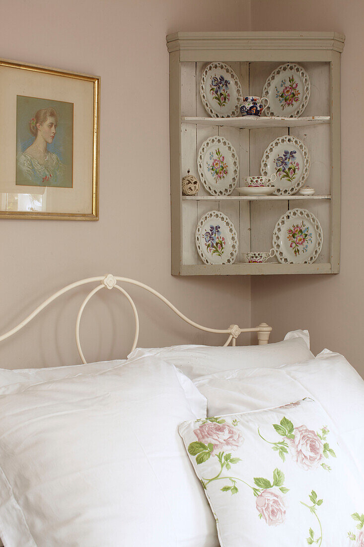 Dekorative Teller auf wandmontiertem Eckregal über dem Bett mit Blumenkissen in Doppelhaushälfte UK