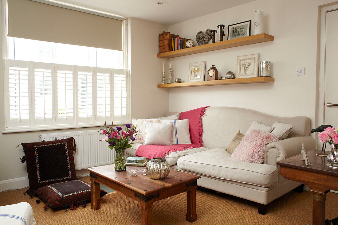 Sofa below wooden shelves with wooden coffee table and floor cushions in living room of semi-detached home UK