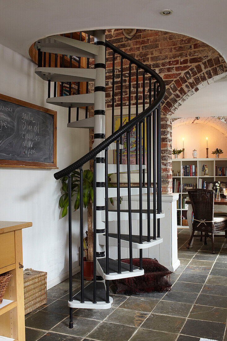 Black spiral staircase with blackboard in tiled open plan interior of semi-detached home UK