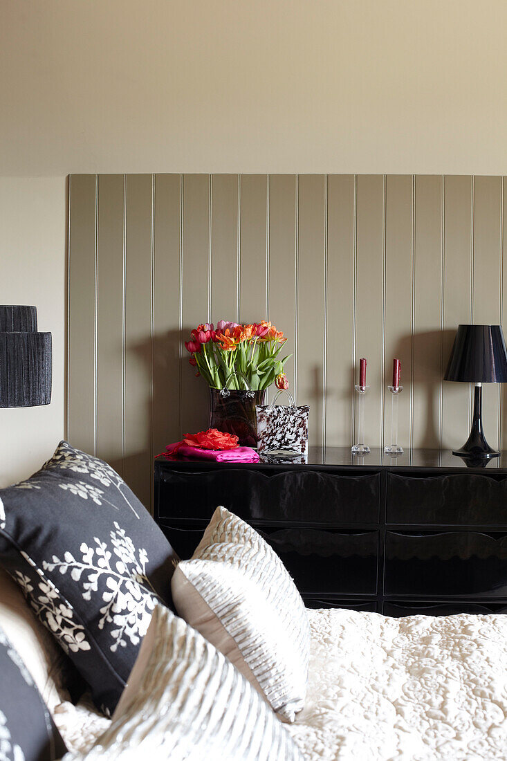 Blumengemustertes Kissen mit schwarzer Anrichte im Schlafzimmer einer umgebauten Scheune in Somerset, England, UK