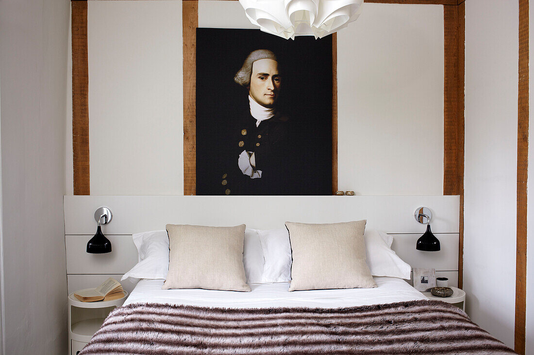 Historic painting above contemporary bed in timber framed cottage in Coombe, England, UK