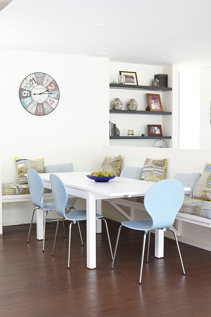Hellblaue Esszimmerstühle am Tisch unter der Uhr in einem modernen Haus auf der Isle of Wight, UK