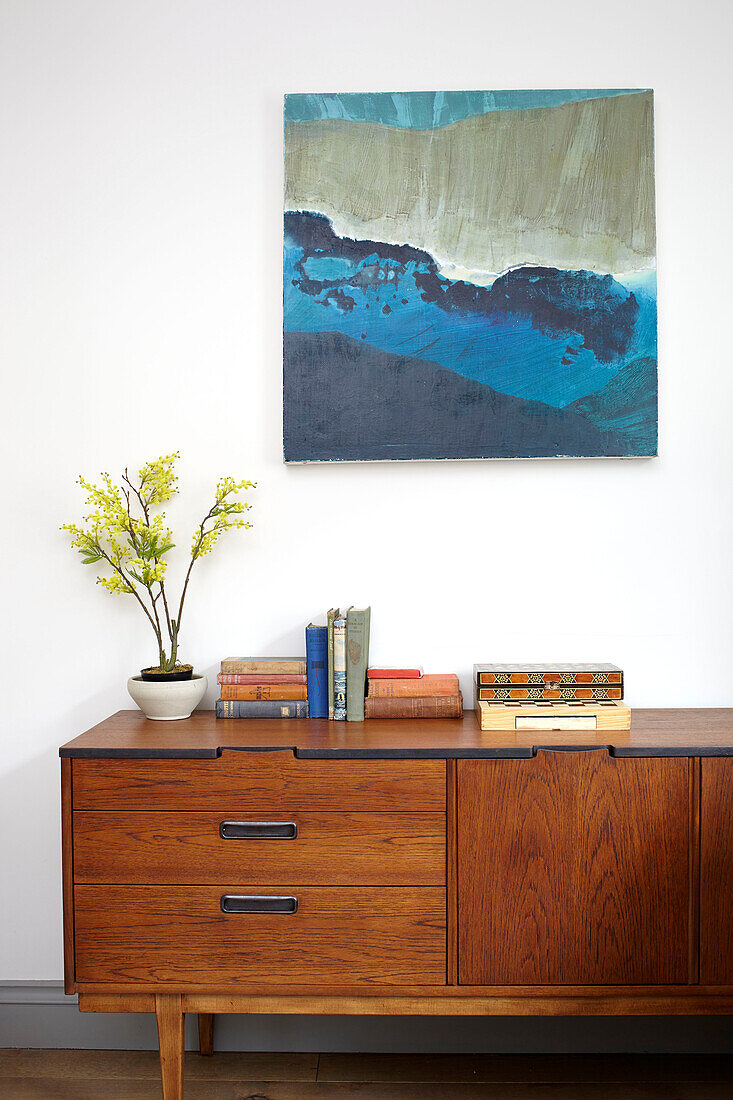 Artwork above books and houseplant on vintage wooden sideboard in Brighton home East Sussex UK