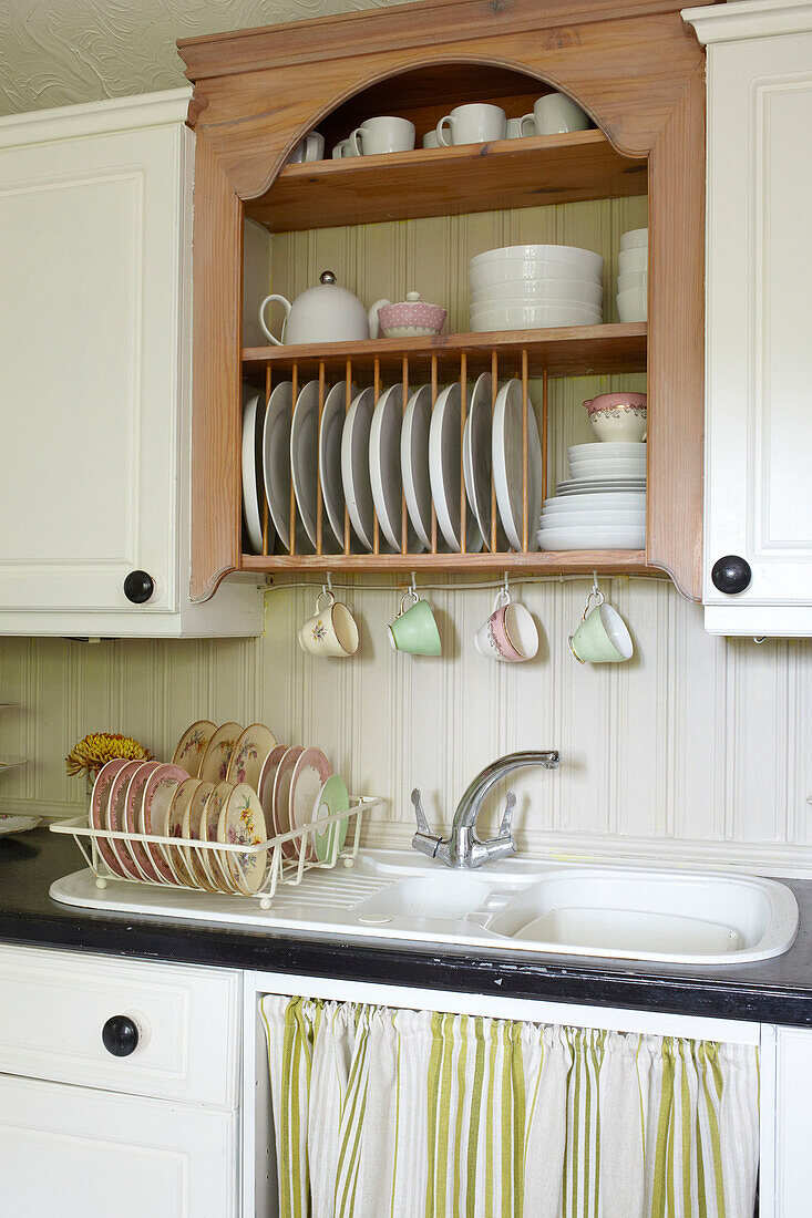 Plate rack and draining board with striped fabric below kitchen sink in East Cowes home, Isle of Wight, UK