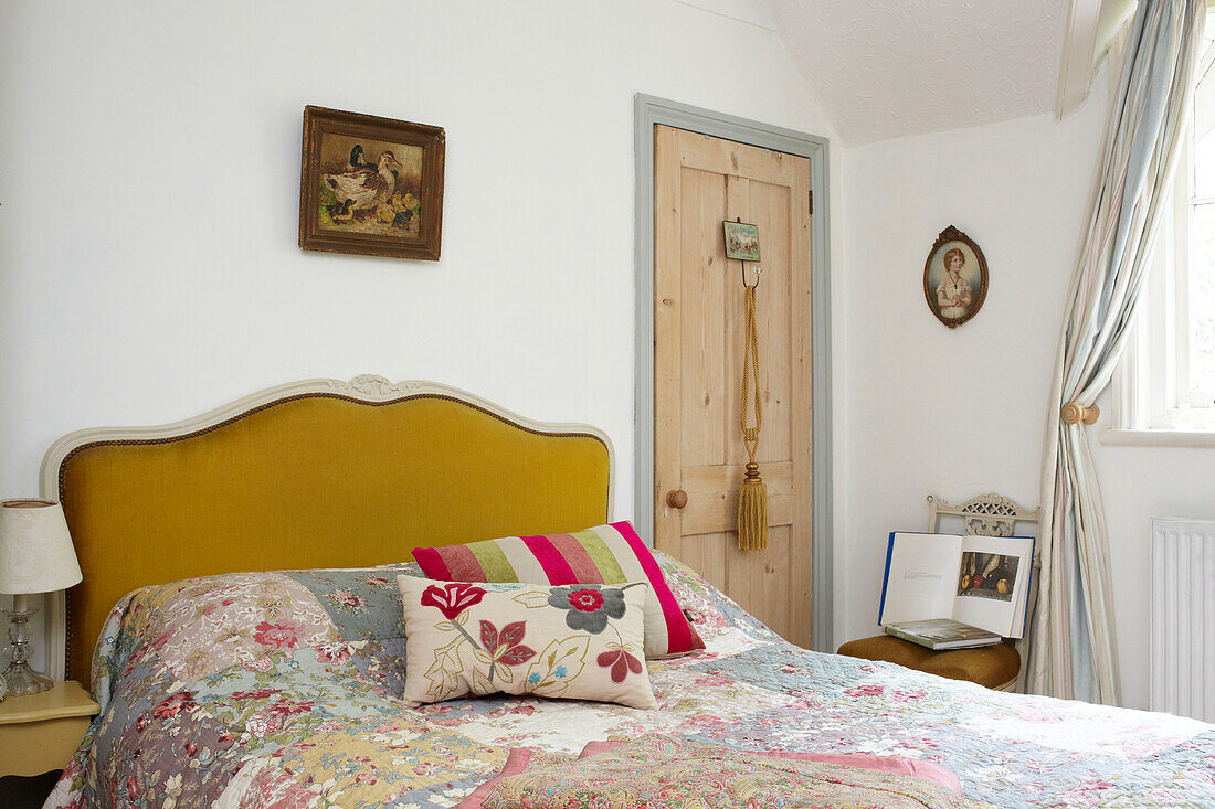 Blumenkissen und Patchworkdecke auf Doppelbett mit senfgelbem Kopfteil in einem Haus in East Cowes, Isle of Wight, UK