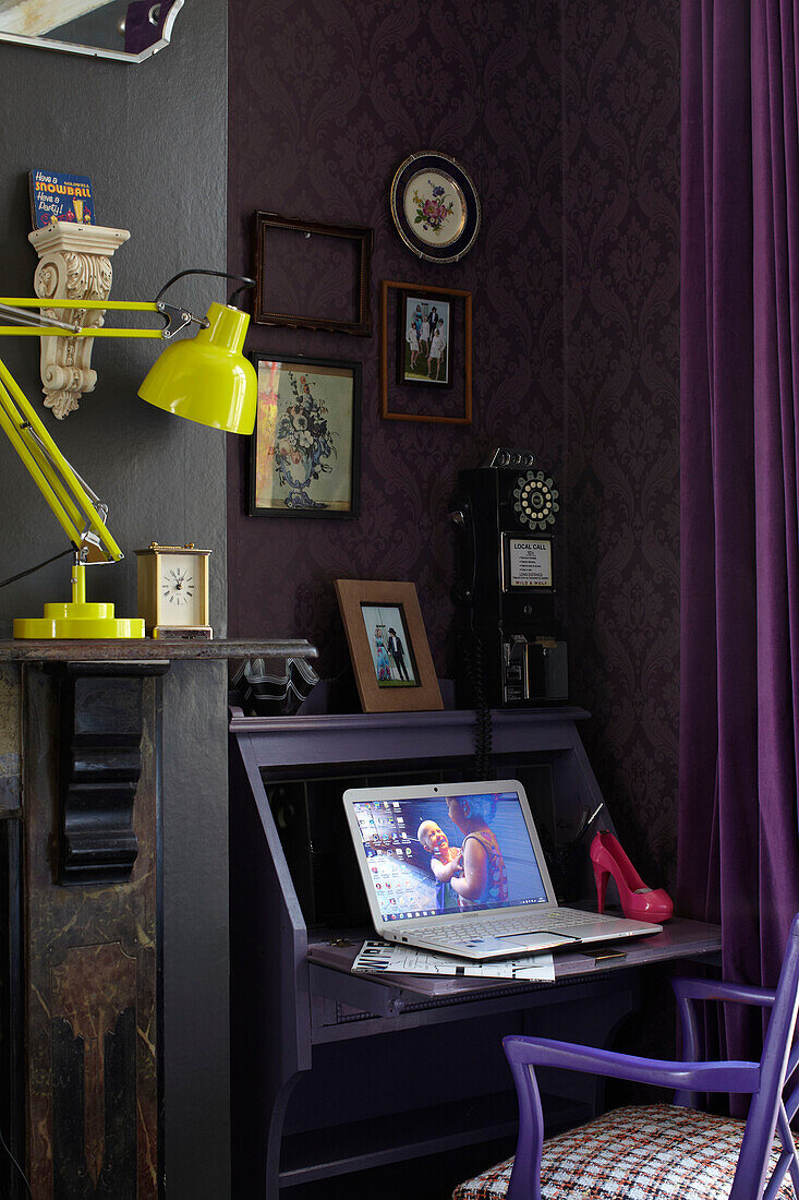 Laptop auf lilafarbenem Schreibtisch mit Stuhl und gelber Schreibtischlampe in einem Haus im Retrostil in London, England, Vereinigtes Königreich