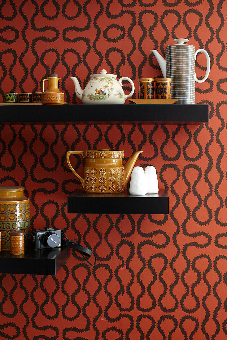 Vintage-Keramik auf schwarzem Regal mit gemusterter Tapete in einem Haus in London, England, UK