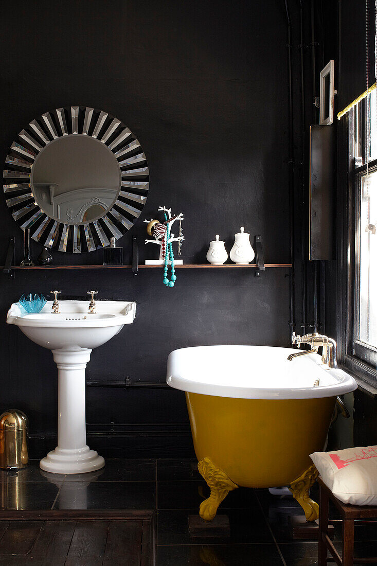 Gelbe freistehende Badewanne mit altem Spiegel und Waschbecken in einem Badezimmer in London, England, UK