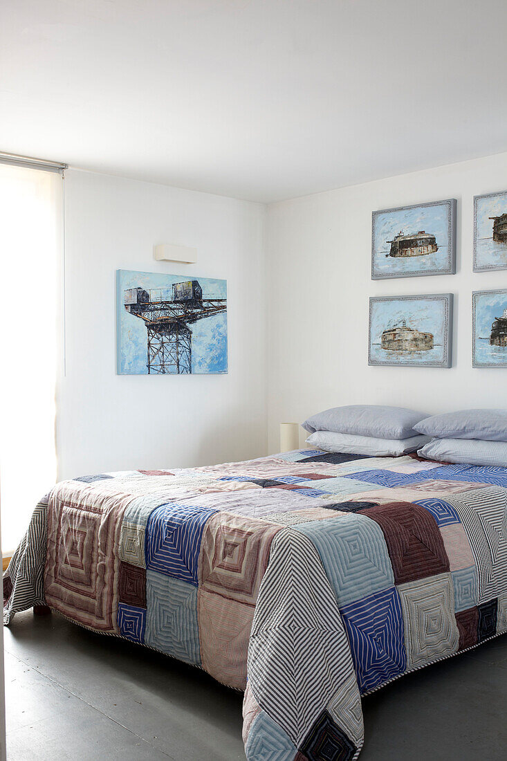Patchworkdecke auf einem Doppelbett mit Kunstwerken in einem Hausboot in Bembridge, Isle of Wight, Großbritannien