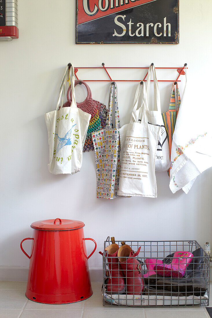Einkaufstüten hängen über einer roten Aufbewahrungsdose und einem Metallkorb mit Kinderschuhen in der Küche von Ryde, Isle of Wight, Großbritannien